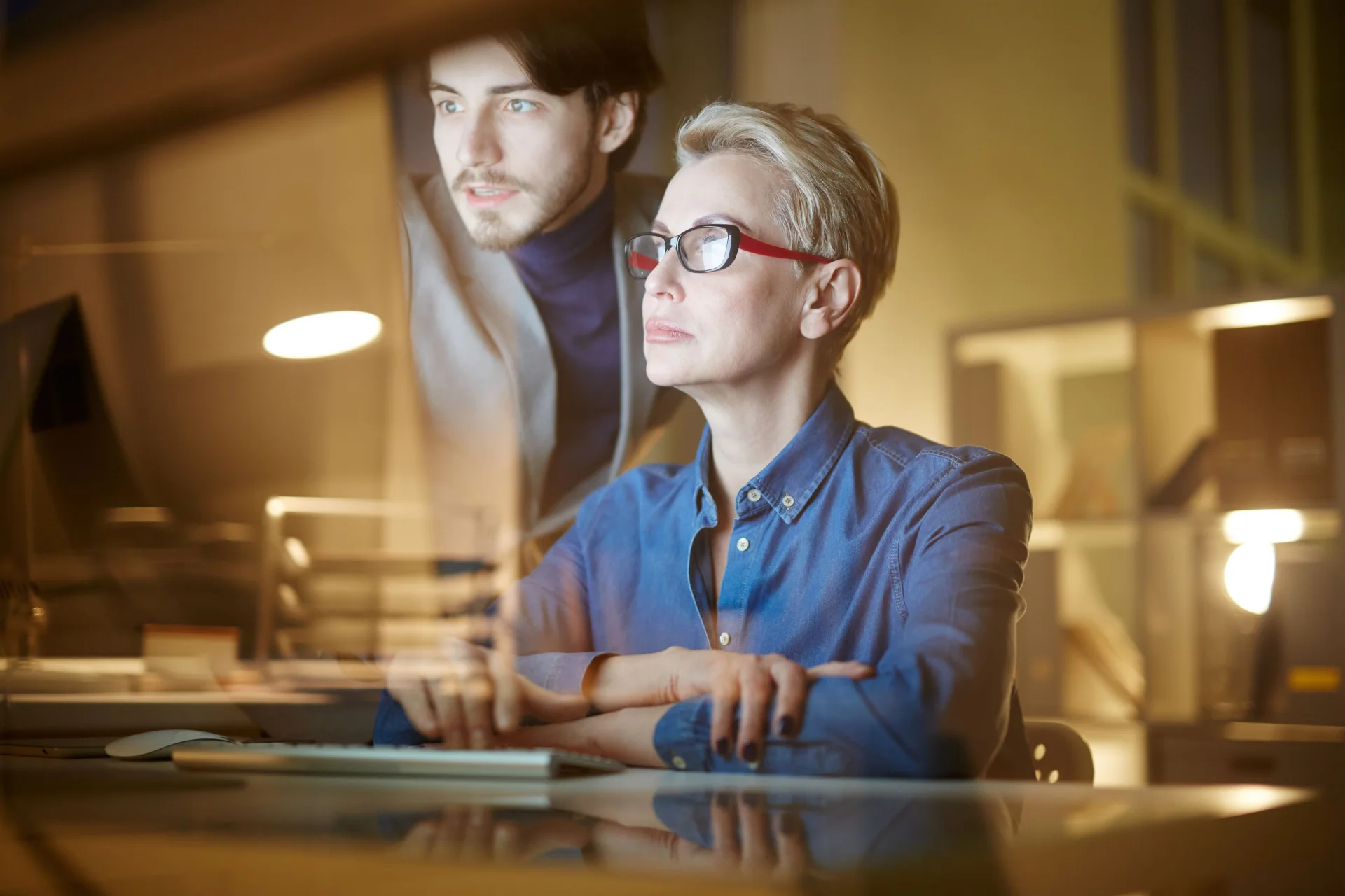 Two colleagues working together at a screen in a dimly lit office