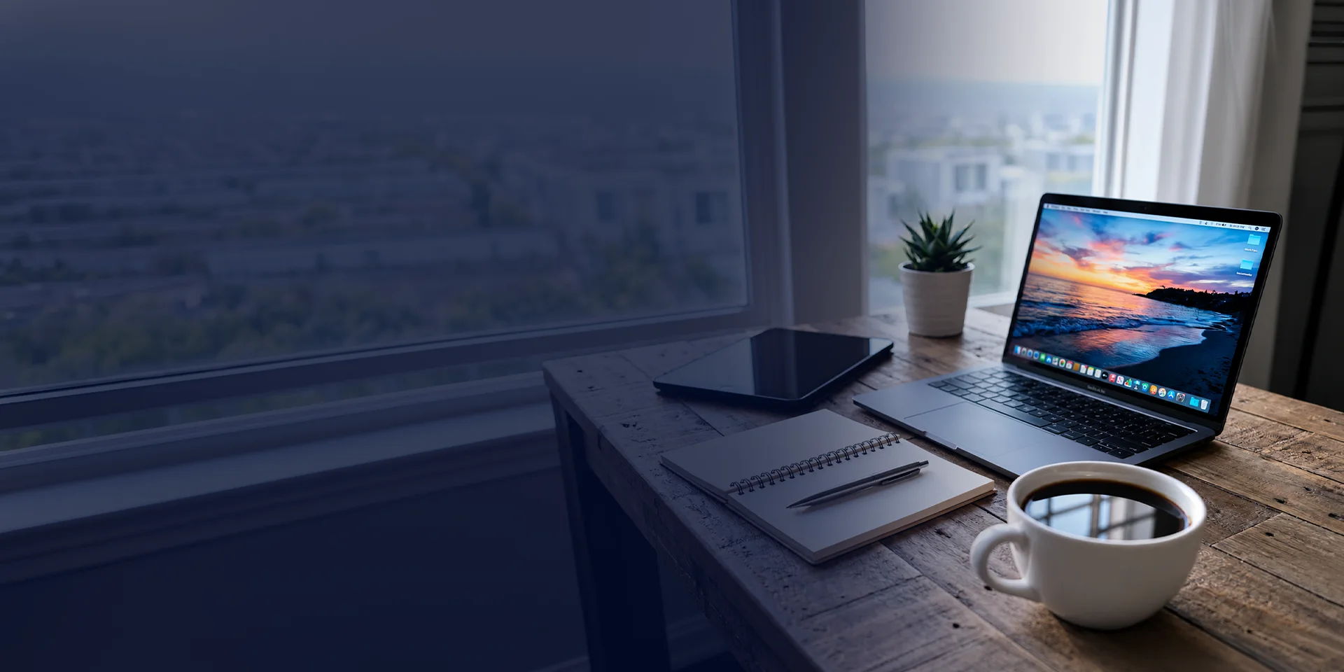 A laptop and notebook on a desk by a window over the city